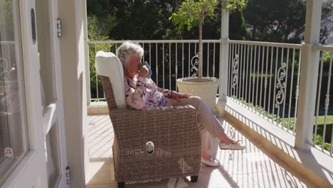 caucasian senior woman drinking coffee while sitting on a chair in the balcony at home