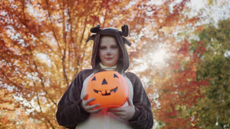 una niña con un disfraz de ciervo sostiene una canasta en forma de calabaza. los niños están listos para recoger dulces el día de halloween