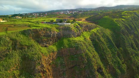 aerial view of house in green cliff on madeira island during sunny day, portugal - orbiting shot