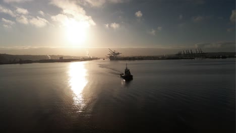 orbiting a tugboat moving across golden sunlight reflecting off calm water, port of tacoma, aerial