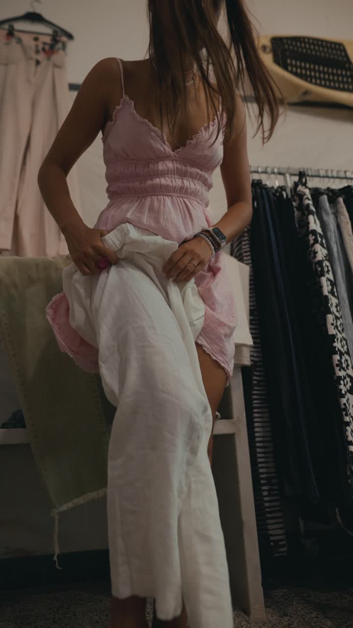 Woman in Pink Dress Holding White Pants in Wardrobe