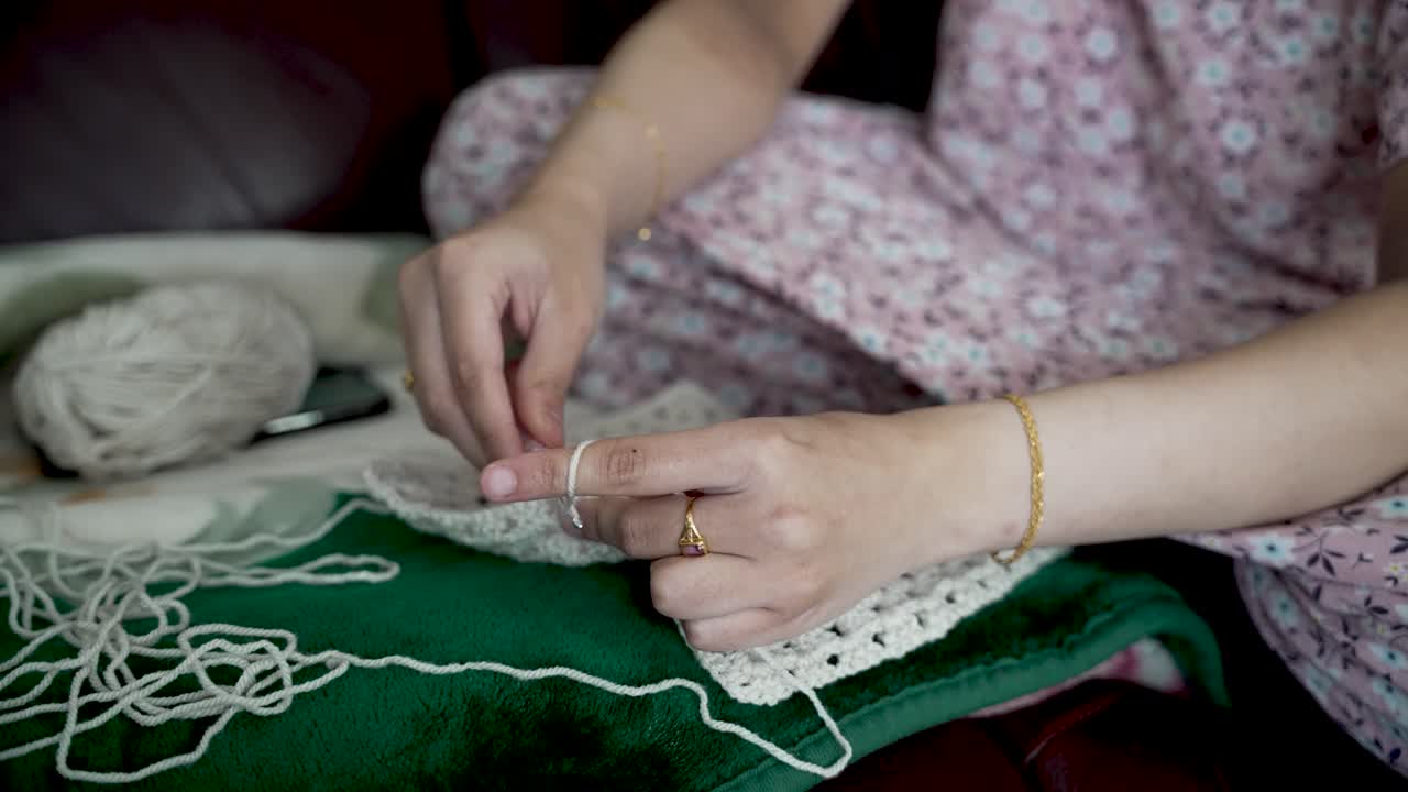 Woman sitting comfortably on a sofa, crocheting with white thread, enjoying a relaxing pastime and expressing her creative skills