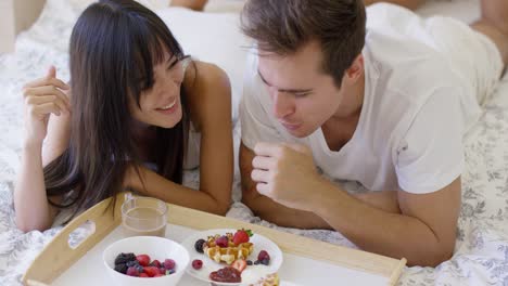 침대에서 과일과 와플 아침 식사를 하는 커플