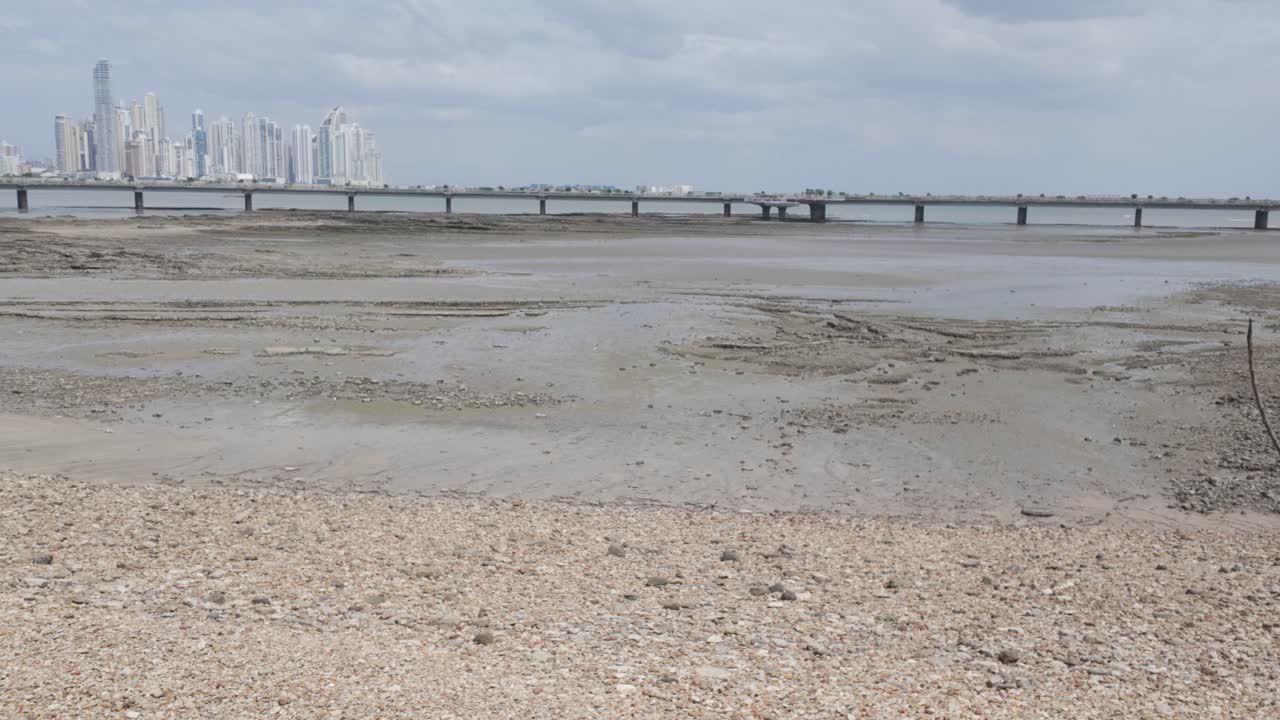 Panama City's Casco Viejo waterfront during low tide with distant bridge and cloudy sky