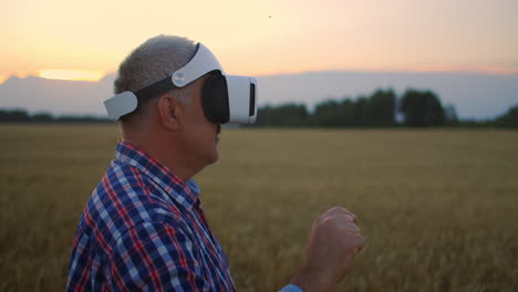 Granjero-Adulto-Mayor-Con-Un-Casco-De-Realidad-Virtual-En-Un-Campo-De-Cultivos-De-Cereales.-A-La-Luz-Del-Atardecer,-Un-Anciano-En-Un-Tractor-Utiliza-Gafas-De-Realidad-Virtual.-Tecnologías-Vr-Y-Agronegocios-Modernos