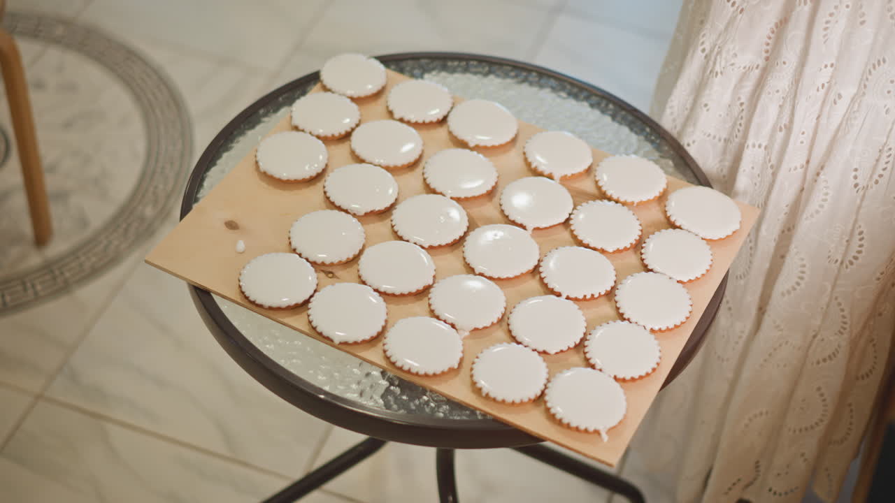 Tray mini pie shells on glass table, morning light casting soft shadows over neat rows of empty tart shells on baking board, round metal stand and tiled floor visible, curtain backdrop, warm neutral