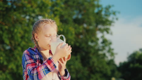 Ein-Mädchen-Trinkt-Milch-Aus-Einem-Glaskrug-In-Ihrem-Garten-Gesundes-Bio-Produktkonzept