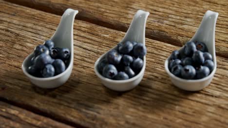 Three-spoons-of-blueberries-arranged-on-wooden-table-4k
