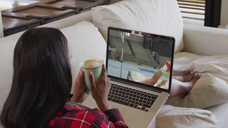 Composite-of-woman-sitting-at-home-holding-coffee-watching-athletics-high-jump-event-on-laptop