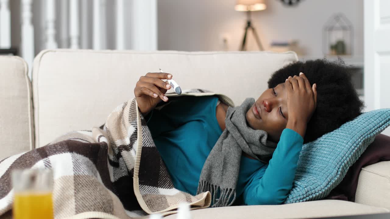 Close up of African American female lying on sofa and looking at termometer