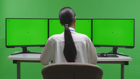 녹색 화면으로 트리플 모니터 설정에서 일하는 여성
