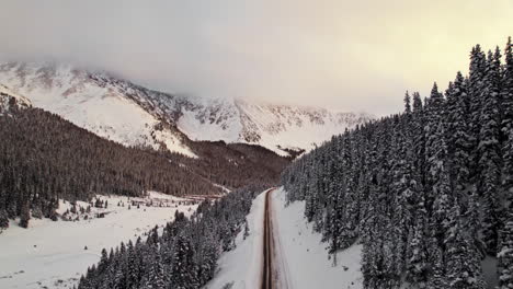 Imágenes-Aéreas-De-Drones-Volando-Sobre-Una-Solitaria-Carretera-De-Montaña-En-El-Valle-De-Las-Montañas-Rocosas-Rodeadas-De-Nieve-Y-Pinos-Durante-La-Hermosa-Puesta-De-Sol-De-La-Hora-Dorada-En-El-Paso-De-Loveland,-Colorado