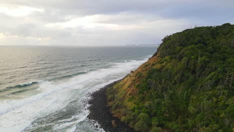 Weiße-Wellen,-Die-An-Den-Füßen-Der-Bewaldeten-Burleigh-landzunge-An-Der-Goldküste,-Queensland,-Bei-Einem-Bewölkten-Sonnenuntergang-Zusammenbrechen