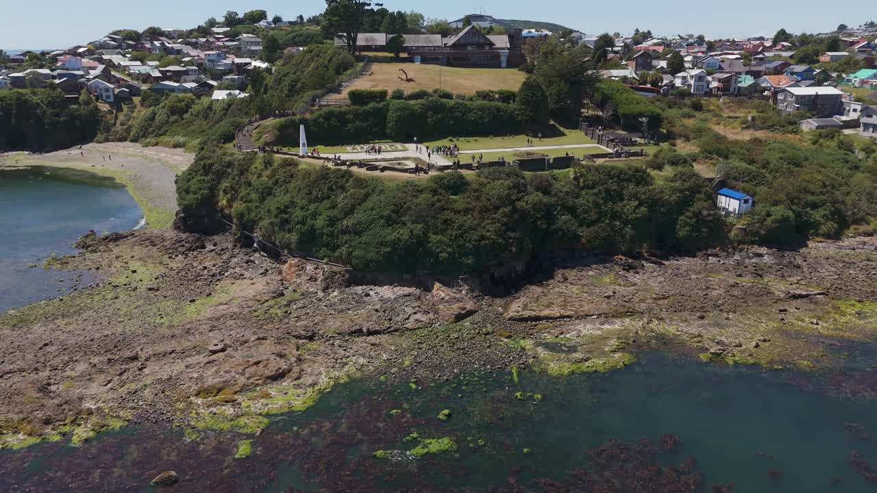 Historical fortress surrounded by lush greenery overlooking the coastline of Ancud, Chiloé. Aerial pull back shot