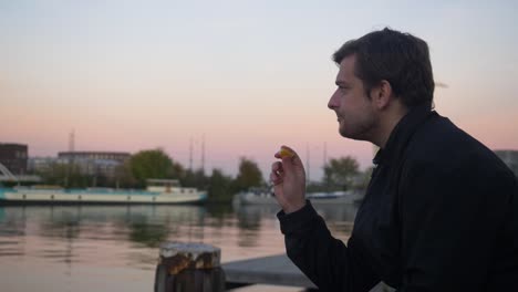 plano amplio de un joven comiendo una rodaja de naranja y sonriendo en un muelle de agua durante la puesta de sol