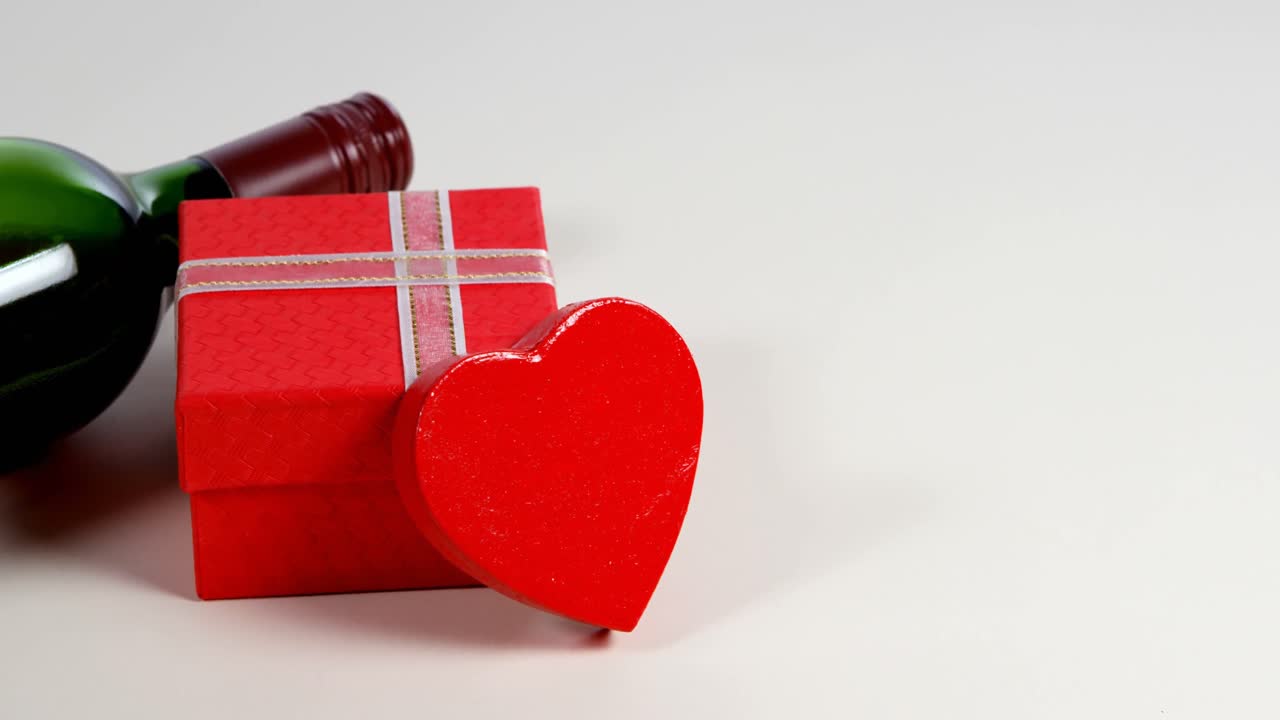 botella de vino, caja de regalo y corazón rojo en superficie blanca 4k