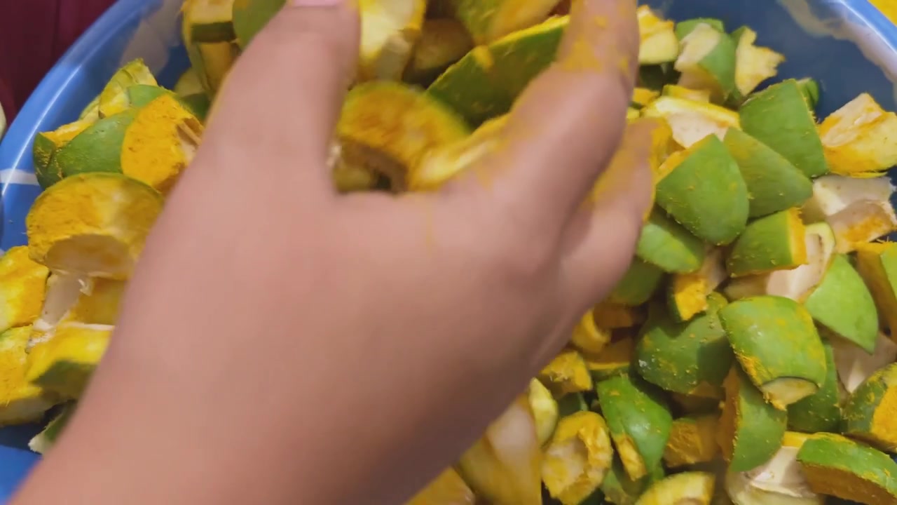 Vista ravvicinata di pezzi di mango crudo tritati mescolati con curcuma e sale durante la preparazione tradizionale di sottaceti fatti in casa per rimuovere l'umidità in eccesso prima della conservazione