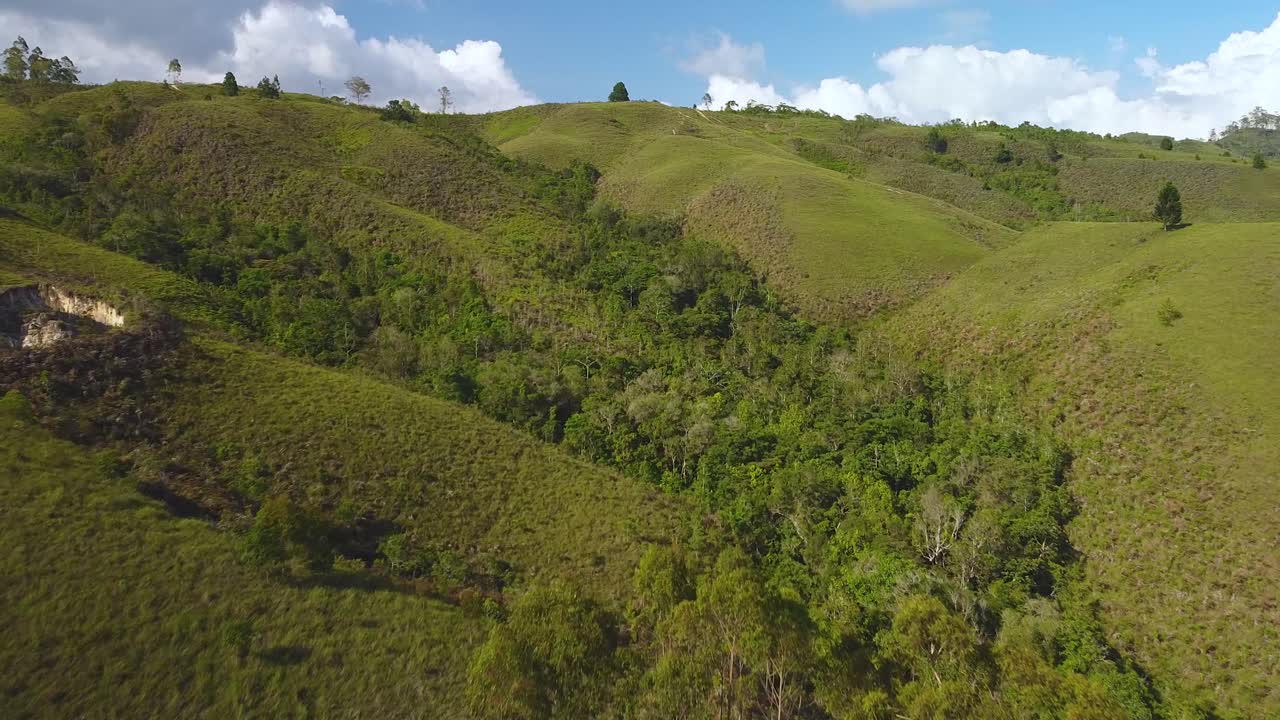 Drone vola in una valle alberata tra le montagne, in un soleggiato tardo pomeriggio.