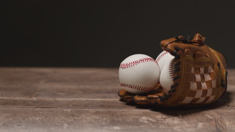 Studio-Baseball-Schuss-Mit-Ball-Im-Fängerhandschuh-Und-Person,-Die-Einen-Holzschläger-Vom-Holzhintergrund-Aufhebt