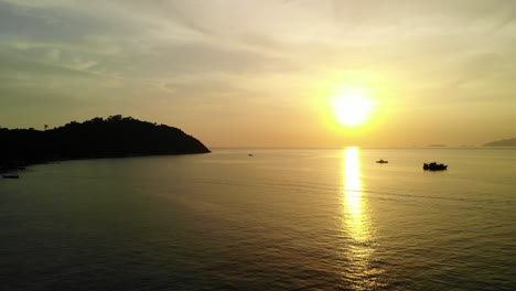 Océano-Tranquilo-Con-Una-Puesta-De-Sol-Dorada,-Barcos-Y-Montañas-Al-Fondo