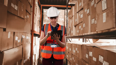 Caucasian-female-worker-wearing-an-organe-high-vest-and-a-hat-checking-boxes,-using-a-tablet