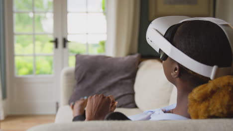 Woman-Relaxing-Lying-On-Sofa-At-Home-Wearing-VR-Headset-And-Interacting-With-AR-Technology