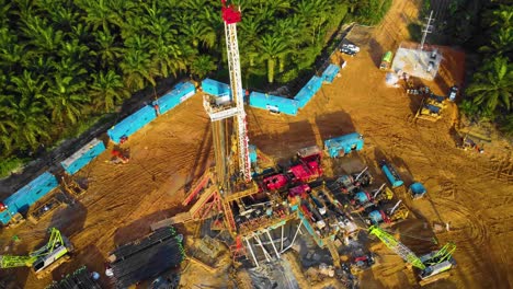 Cinematic-4K-Drone-Footage-of-Onshore-Drilling-Rig-equipment-structure-for-oil-exploration-and-exploitation-in-the-middle-of-jungle-surrounded-by-palm-oil-trees-during-sunset-and-high-oil-price