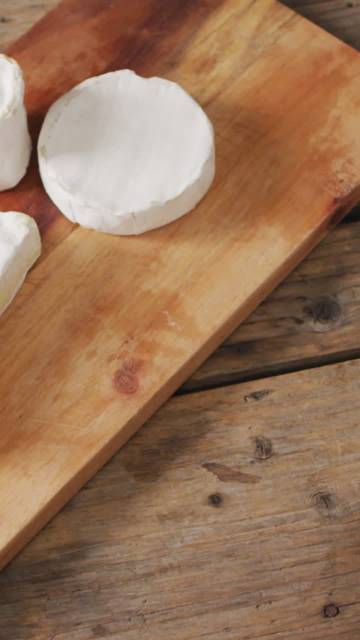 Video overhead shot of assorted soft cheeses on chopping board, on wooden table with copy space