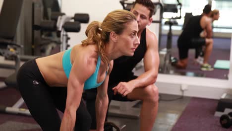 mujer levantando una barra con su entrenador en una sesión de crossfit