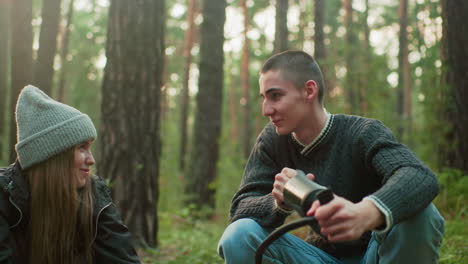 young man wearing green sweater focuses on pumping air as he glances at someone nearby, engaging in outdoor task with soft natural background and relaxed interaction