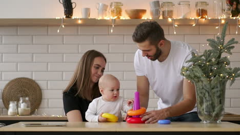 family, holidays and people concept - happy mother, father and little daughter playing with ring pyramid baby toy on birthday party