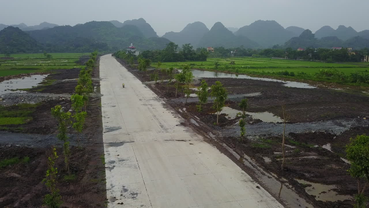 A panoramic view of a road stretching through plantations in the Ninh Binh region of Vietnam. Captures the scenic landscape with rice paddies, greenery, and distant mountains.