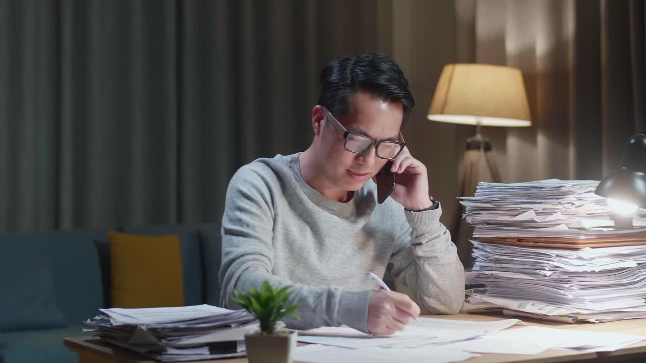 亚洲男子在家工作时，一边打电话一边做笔记
