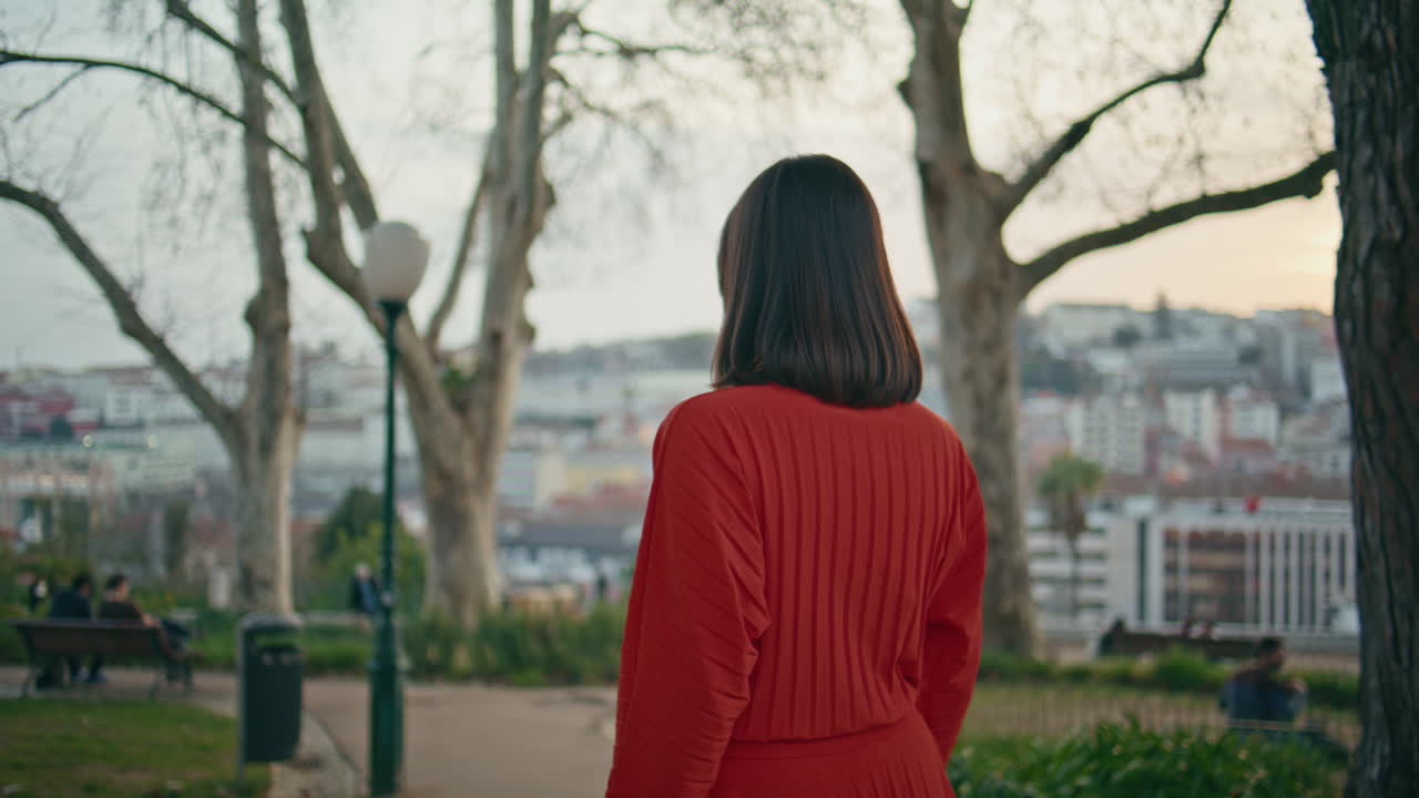 Red dress woman walking park alone back view. Relaxed model girl touching hair
