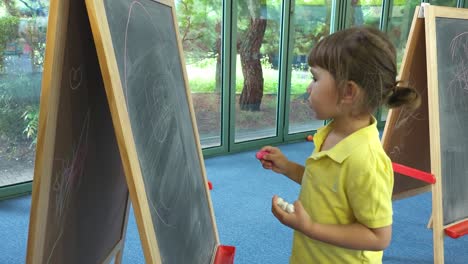 3-Year-Old-Little-Girl-Drawing-with-Chalk-on-Board-Indoors