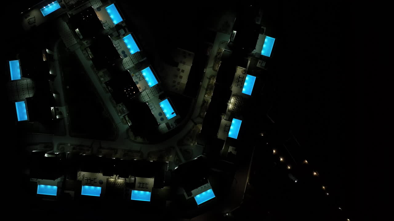 Birds eye drone shot over night lit pools and villas at a resort in Greece