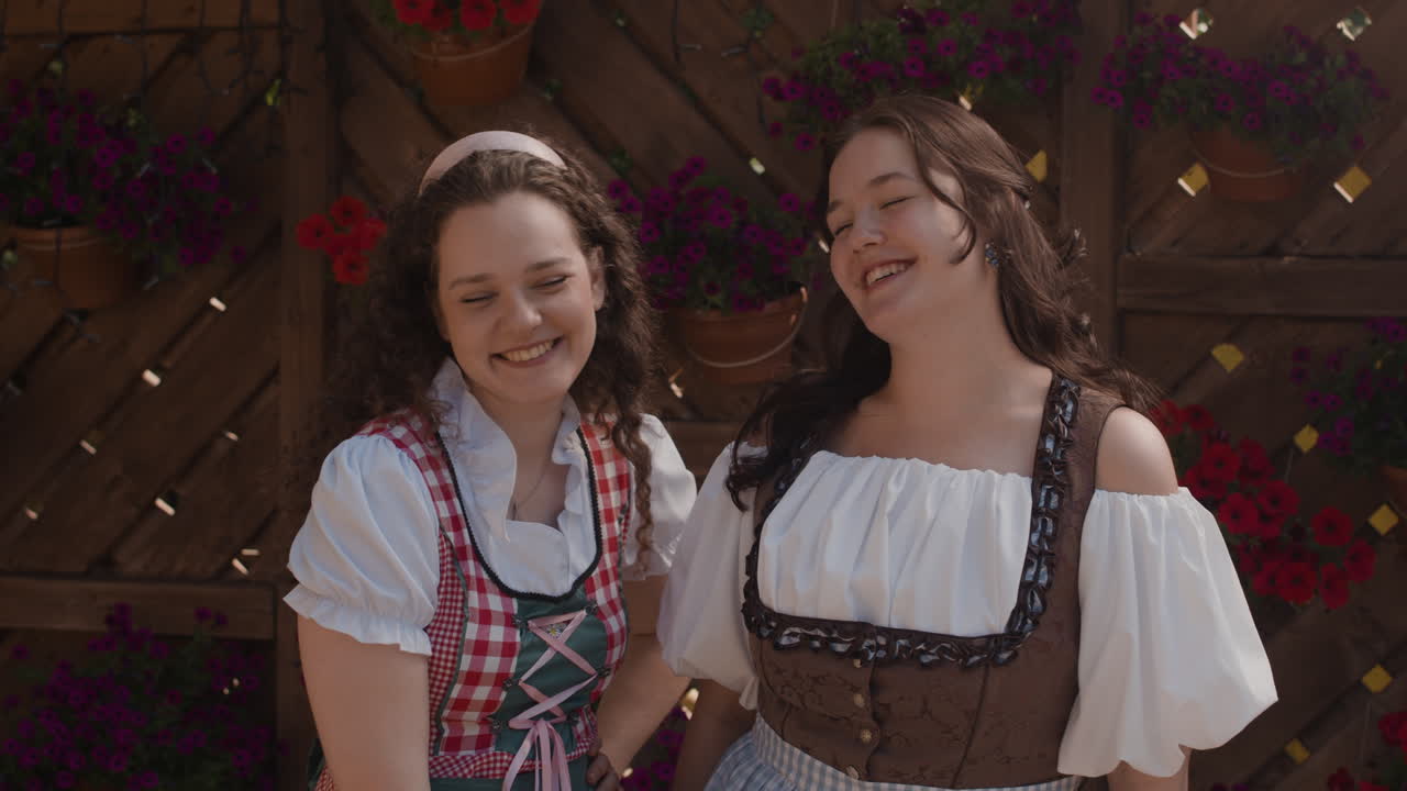 Two women in dirndls smiling in front of a flower-covered fence