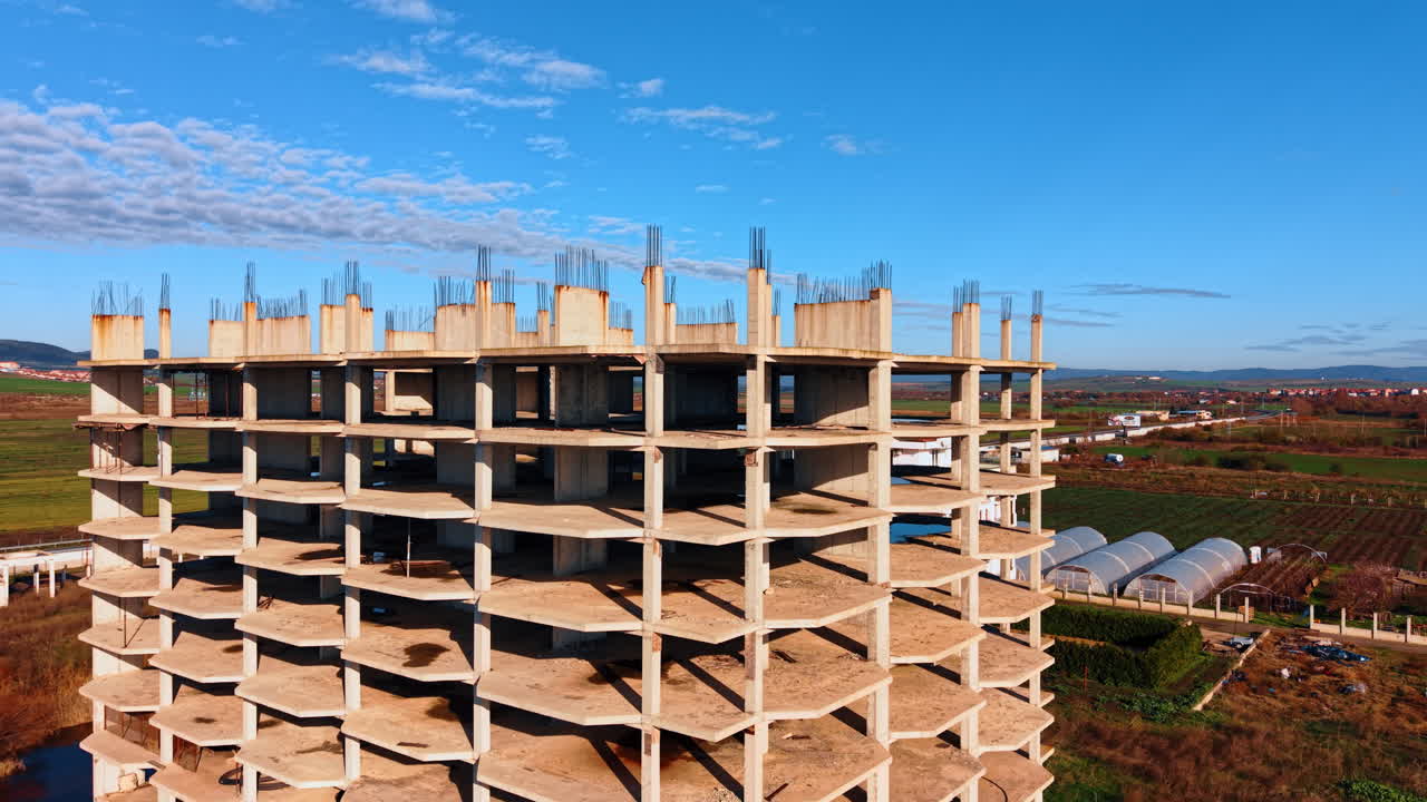 Distancing from a multi-storied frame of the building under construction. Metal rebars stick out from the concrete columns