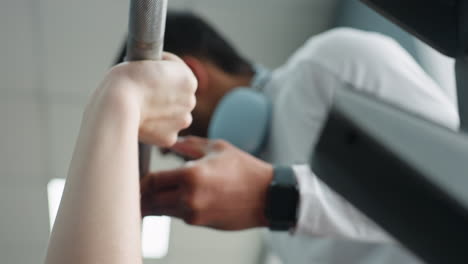 close up of gym instructor in white top assisting someone lifting barbell with blurred depth of field, barbell in sharp foreground while coach slightly out of focus