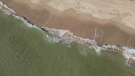 aerial shot of clear ocean small waves crashing on a white sand beach