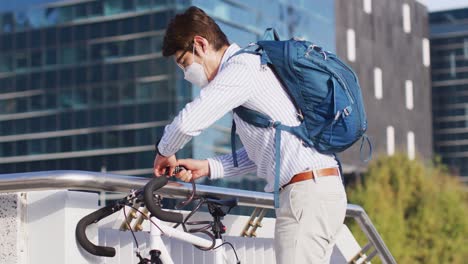 Hombre-Asiático-Con-Mascarilla-Bloqueando-Su-Bicicleta-En-El-Parque-Corporativo