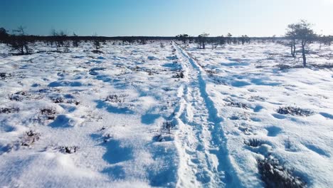 Luftaufnahme-Einer-Verschneiten-Moorlandschaft-Mit-Wanderweg-Und-Zugefrorenen-Seen-An-Sonnigen-Wintertagen,-Dunika-Torfmoor,-Weitwinkel-Drohnenaufnahme,-Die-Sich-Tief-Zum-Wanderweg-Bewegt