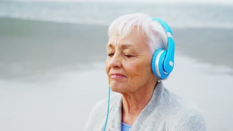 Senior-woman-listening-music-on-headphone-on-beach