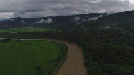aerial moving backwards on muddy jungle river with foggy mountains in background, 4k