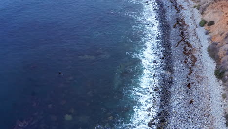 scenic and picturesque view of ocean waves breaking along a rocky shoreline - tilt up descending aerial reveal