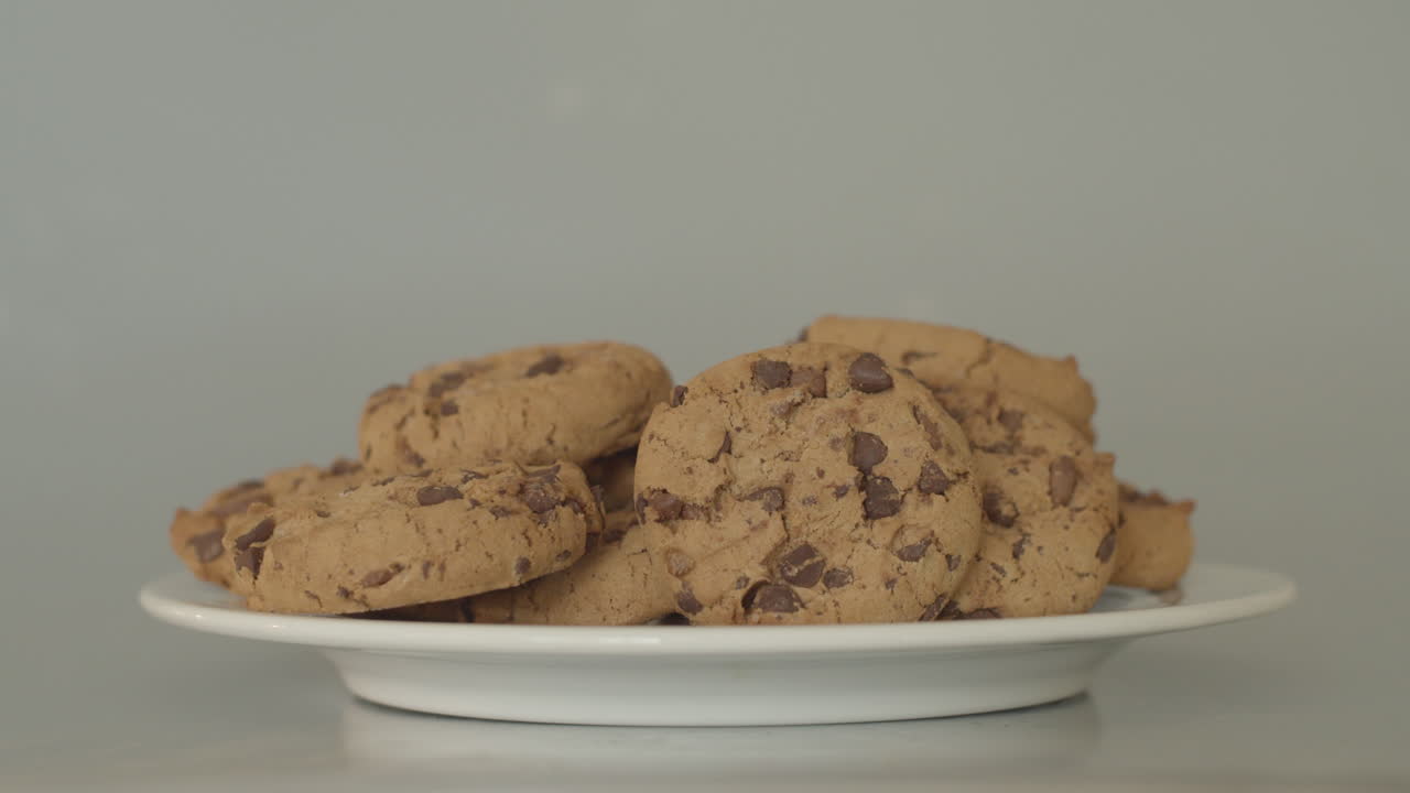 Mano colocando galletas con chispas de chocolate en un plato blanco.