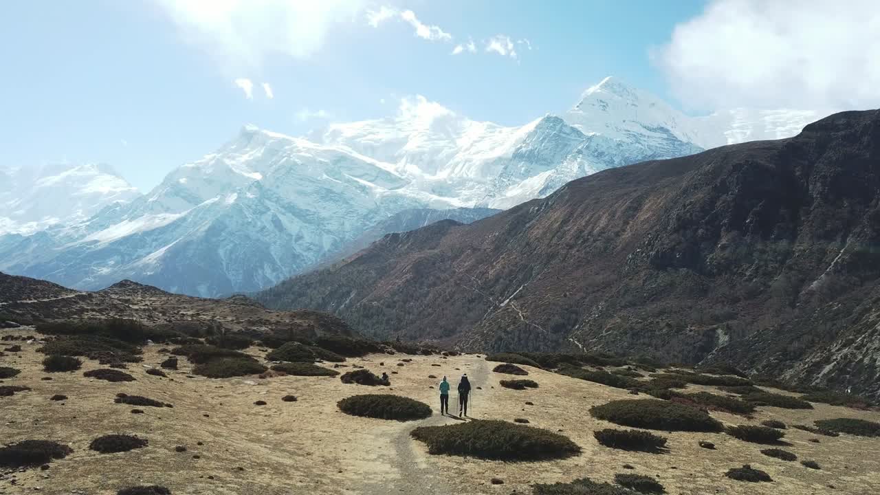 una pareja de senderismo en el valle de manang, annapurna circus trek, himalaya, nepal, con vistas a la cadena de annapurna y gangapurna. paisaje seco y desolado. altos picos de montaña, cubiertos de nieve.