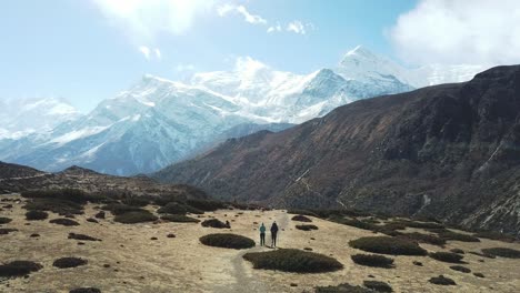 a couple trekking in the manang valley, annapurna circus trek, himalayas, nepal, with the view on annapurna chain and gangapurna. dry and desolated landscape.  high mountain peaks, covered with snow.