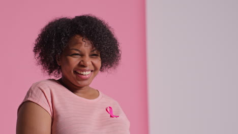 studio portrait of smiling mid adult woman wearing pink breast cancer awareness ribbon against pink background