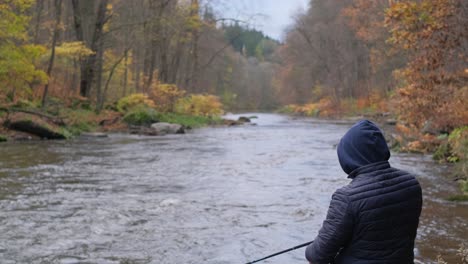 a man in a black jacket is fishing in a forest rushing river against the autumn landscape a man in a black jacket is fishing in a forest rushing river against the background of a beautiful autumn landscape fishing in a mountain river